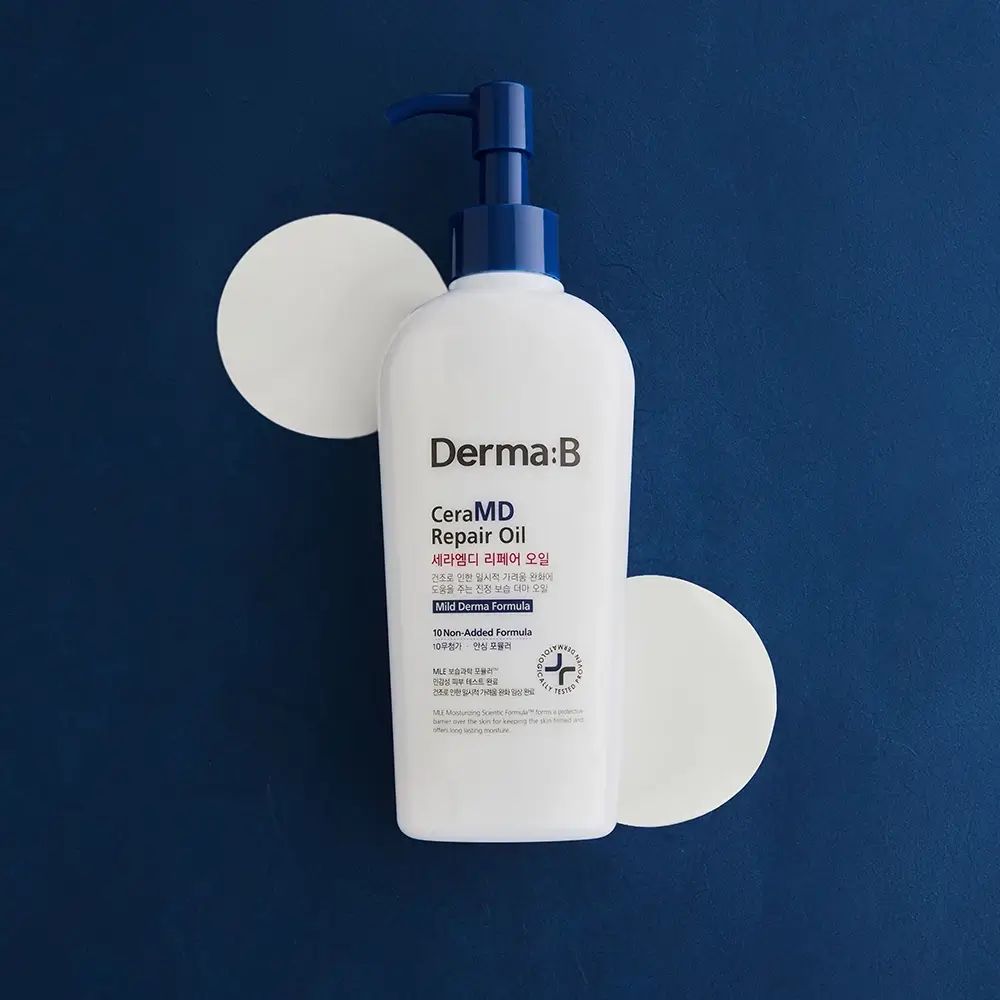 Witte fles met blauwe pomp, omringd door twee witte cirkels. Opschrift: Derma:B CeraMD Repair Oil.