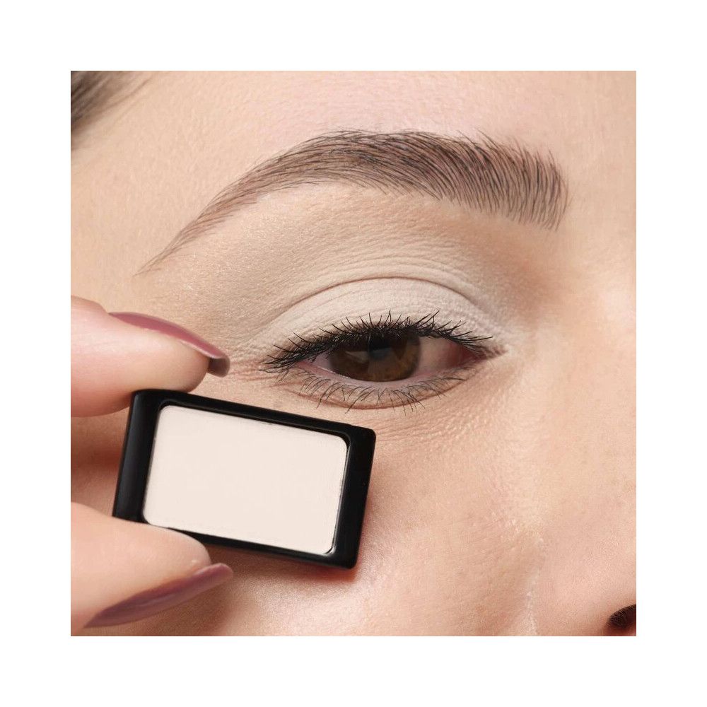 Fard à paupières dans un emballage noir et blanc, tenu par une main, à côté d'un œil. Nom du produit non visible.