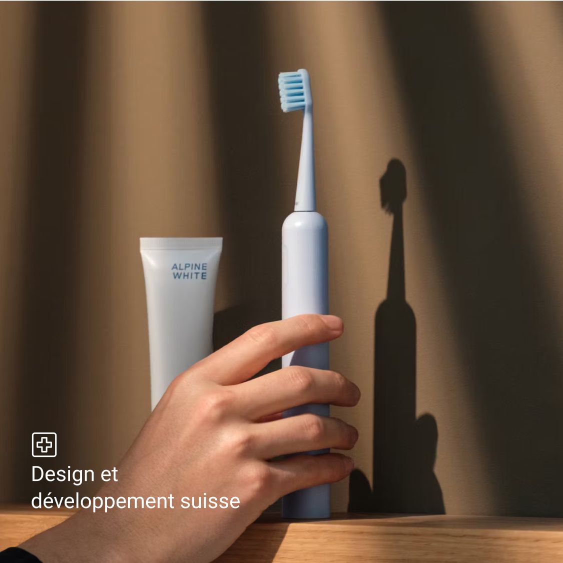 Une brosse à dents électrique bleue, du dentifrice et une main. Design et développement suisses.