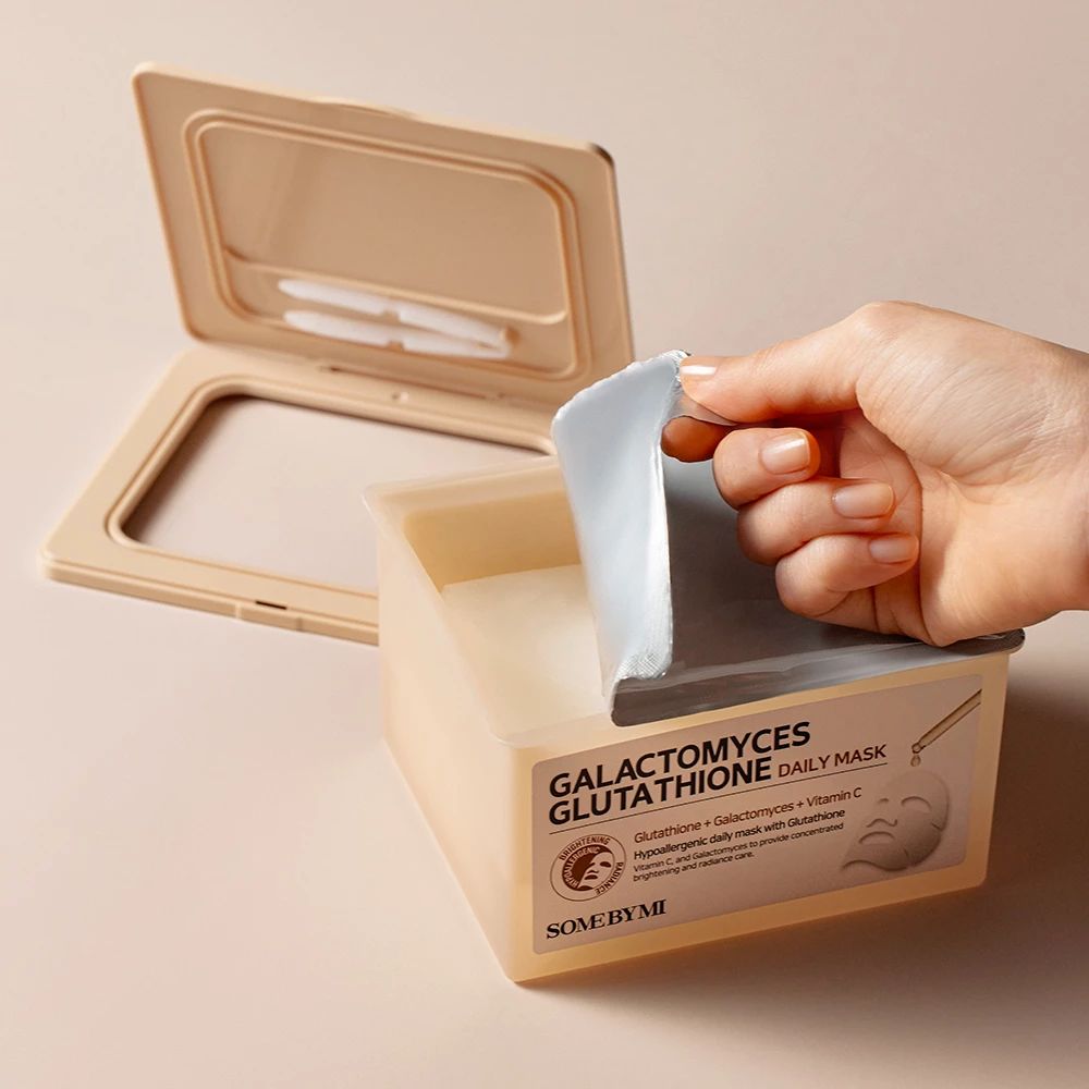 Boîte beige, couvercle ouvert. Main retirant un masque. Inscription : Galactomyces Glutathione Daily Mask.