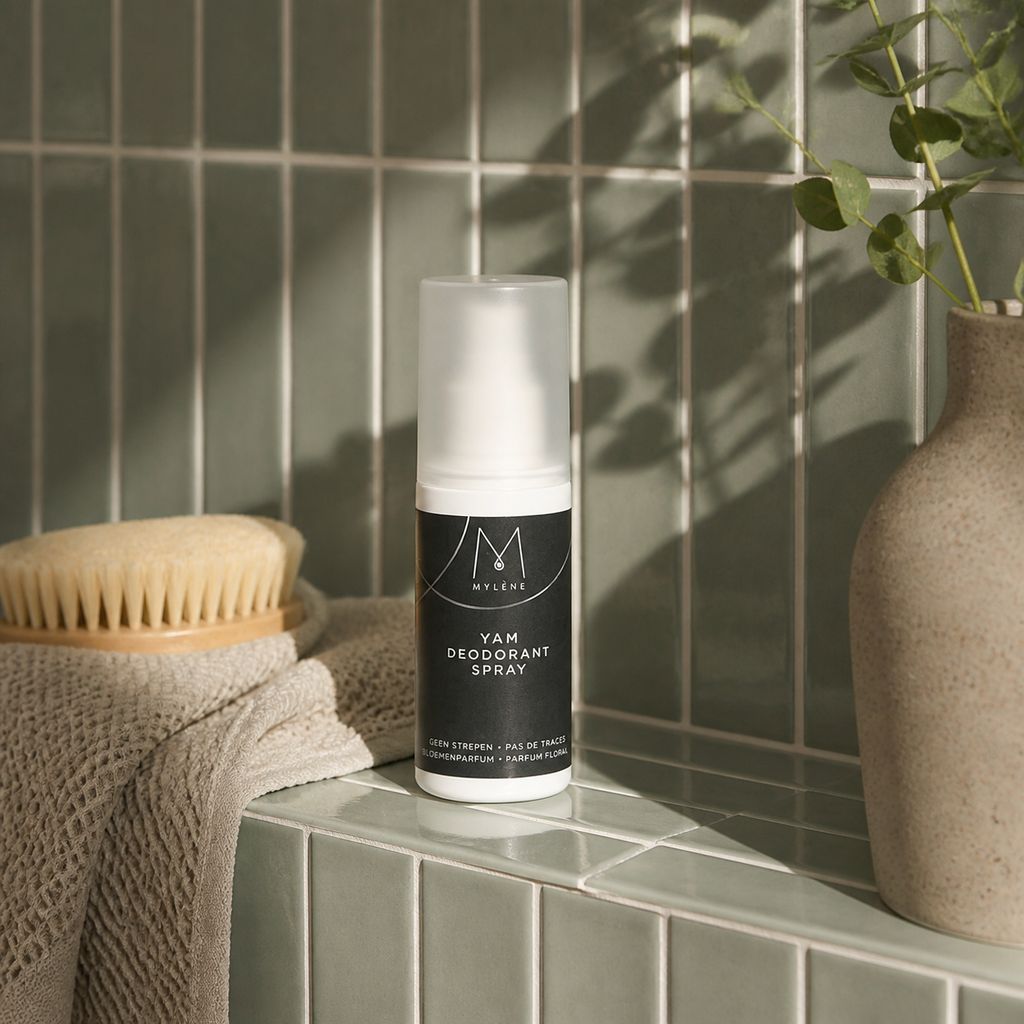 Spray déodorant Mylène Yam à côté d'une brosse et d'une serviette dans une salle de bain.