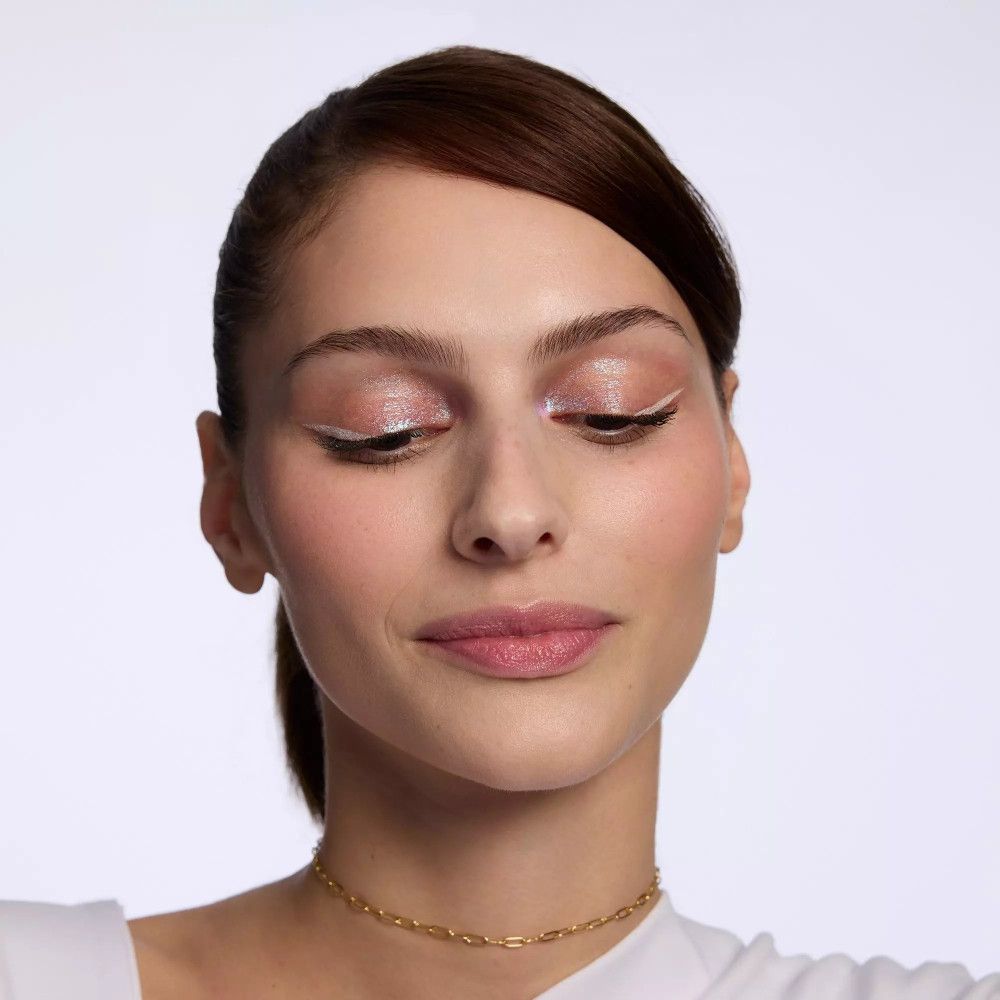 Gros plan d'une femme avec fard à paupières clair et eye-liner blanc. Collier doré. Cheveux brun foncé.