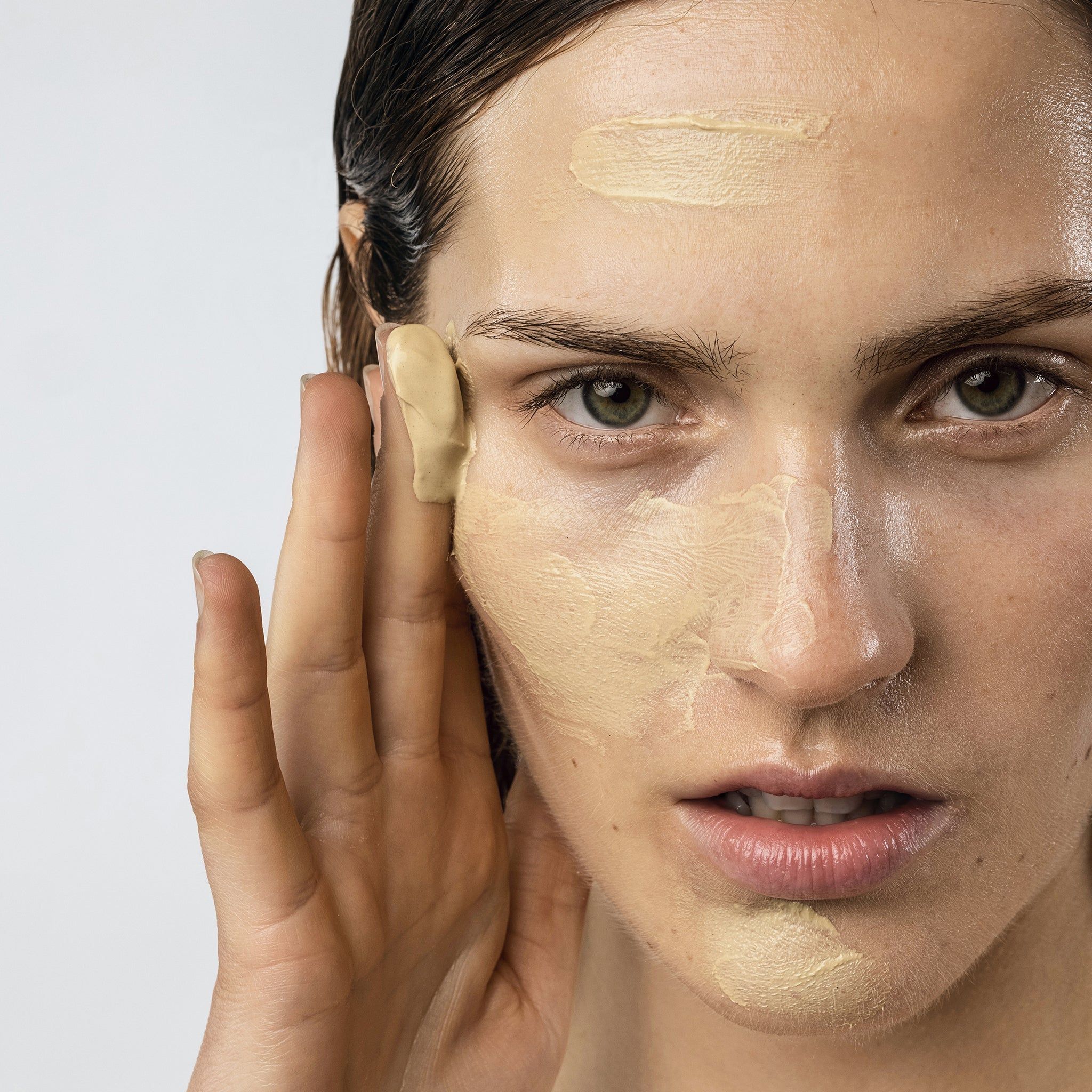 Close-up van een vrouw die een gezichtsmasker aanbrengt. Masker op één kant van het gezicht. Lichte huid.