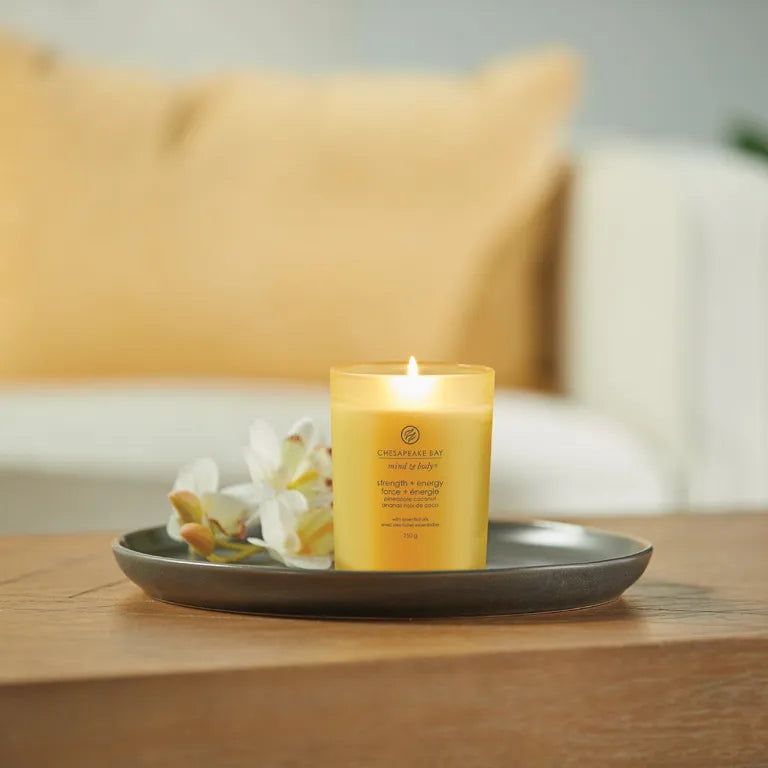Brandende gele kaars op een dienblad met bloemen. Tekst: Chesapeake Bay, mind & body, strength + energy, 250 g.