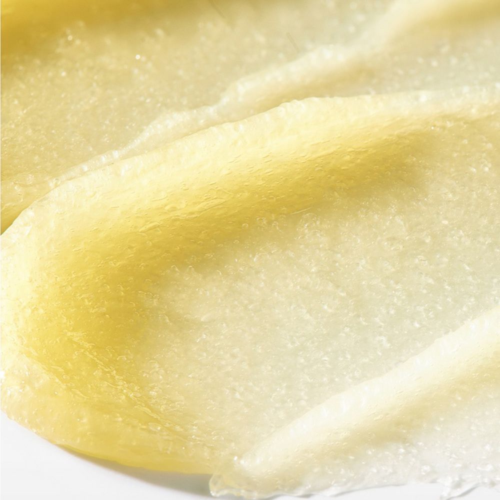 Close-up van een gele, romige substantie met een korrelige textuur, vermoedelijk een lipscrub.