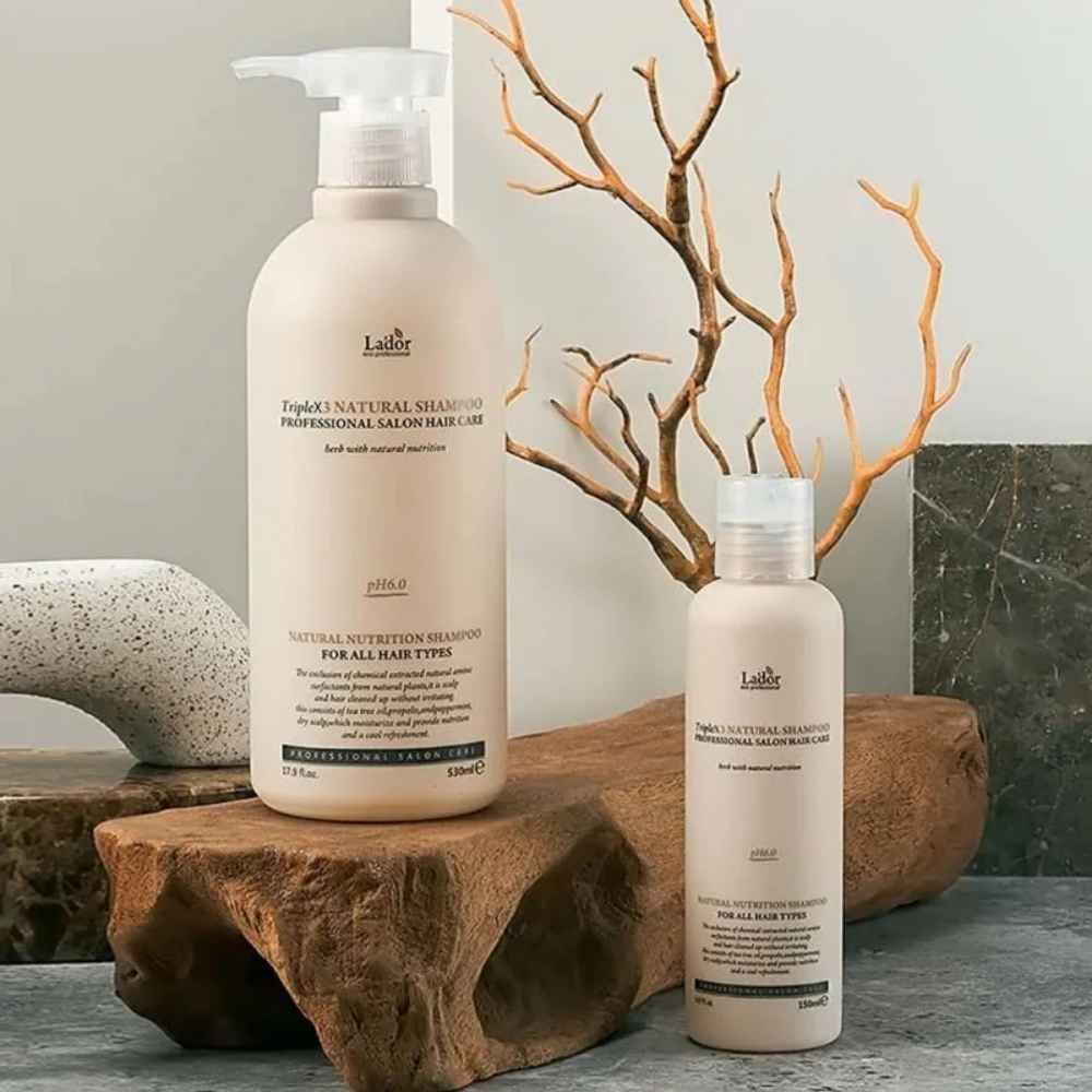 Twee flessen TripleX3 Natural Shampoo, professionele haarverzorging, gerangschikt op hout en steen.