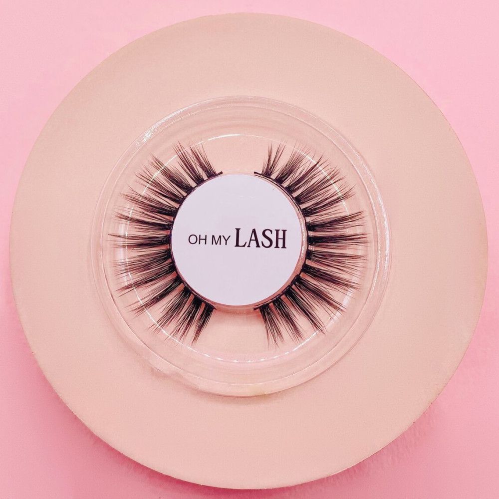 Valse wimpers op roze achtergrond. Ronde, transparante verpakking. Opschrift "OH MY LASH".