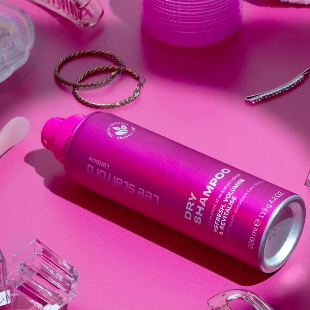 Roze Lee Stafford London Dry Shampoo fles op roze achtergrond. Opschrift: Dry Shampoo. Vegan, dierproefvrij. Met accessoires.