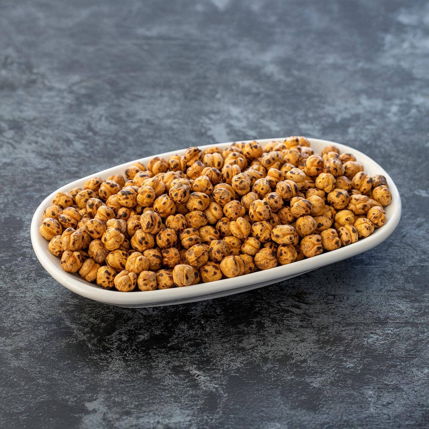 Pois chiches grillés dans un bol ovale blanc sur fond sombre.
