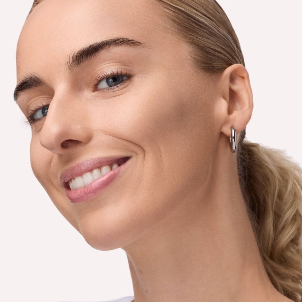 Portrait d'une femme au teint clair. Elle porte des boucles d'oreilles. Son visage est légèrement contouré.