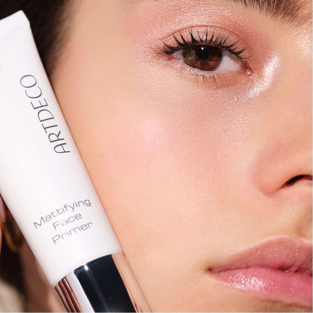 Close-up van een gezicht met witte tube. Opschrift ARTDECO en Mattifying Face Primer. Huid glanzend.