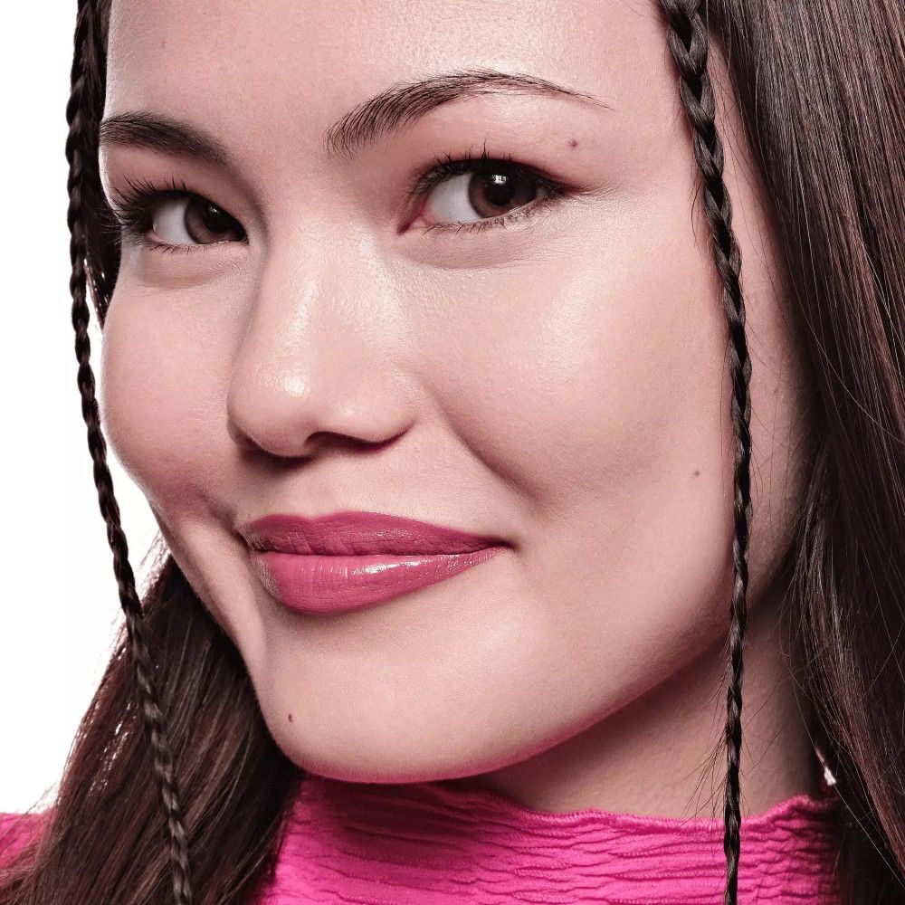 Portrait d'une femme avec du rouge à lèvres rose. Elle a de longs cheveux foncés et des tresses.