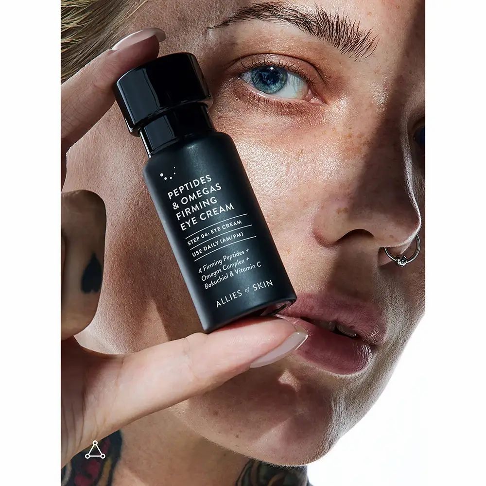 Persoon houdt zwarte fles vast. Tekst: Peptides & Omegas Firming Eye Cream. ALLIES OF SKIN.