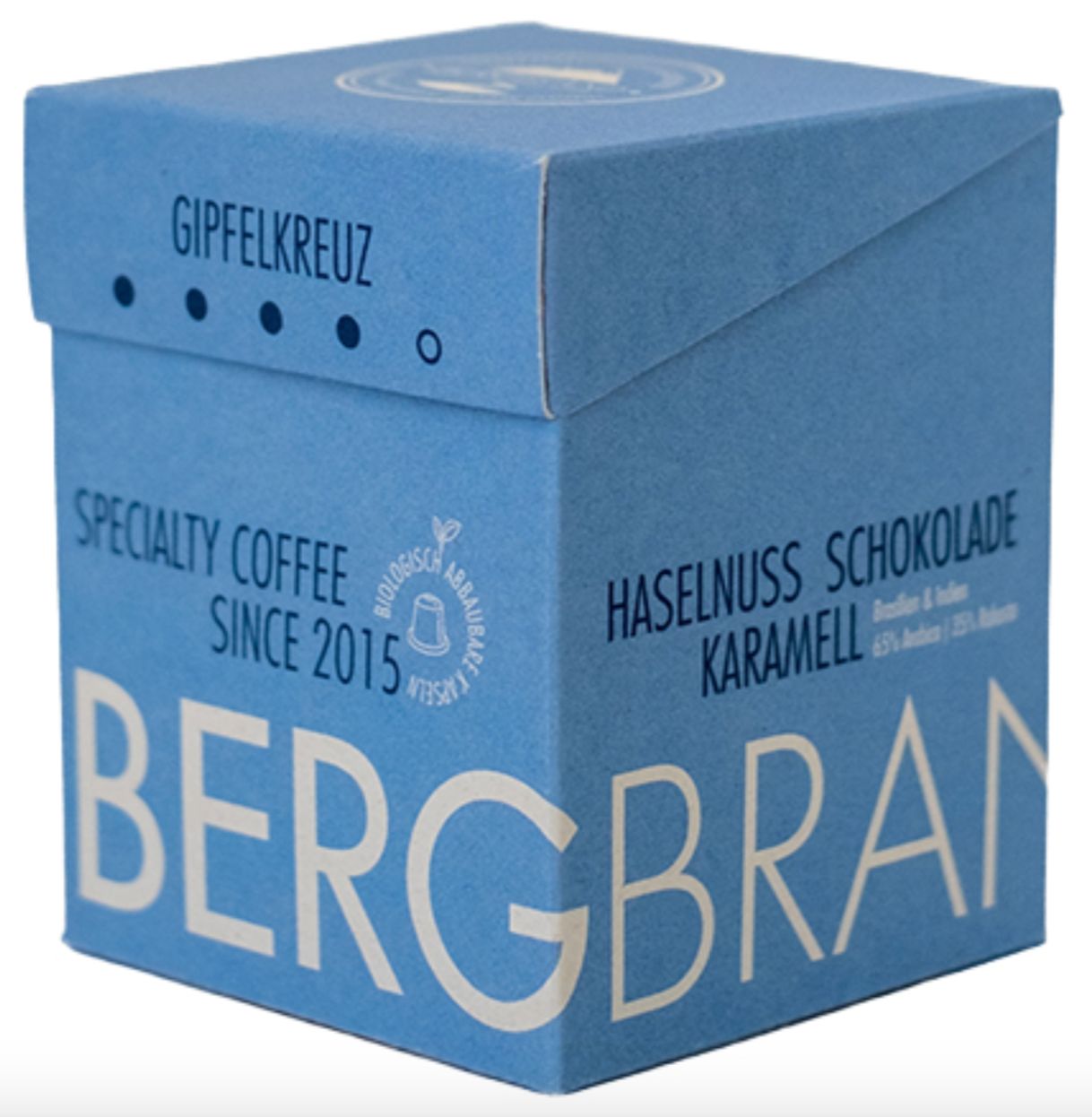 Blauwe doos met BERGBRAND-logo, Gipfelkreuz, Specialty Coffee. Tekst: Hazelnoot Chocolade, Karamel.