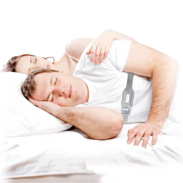 Homme dormant sur le dos, portant une sangle anti-ronflement grise. Femme à côté. Sur literie blanche.