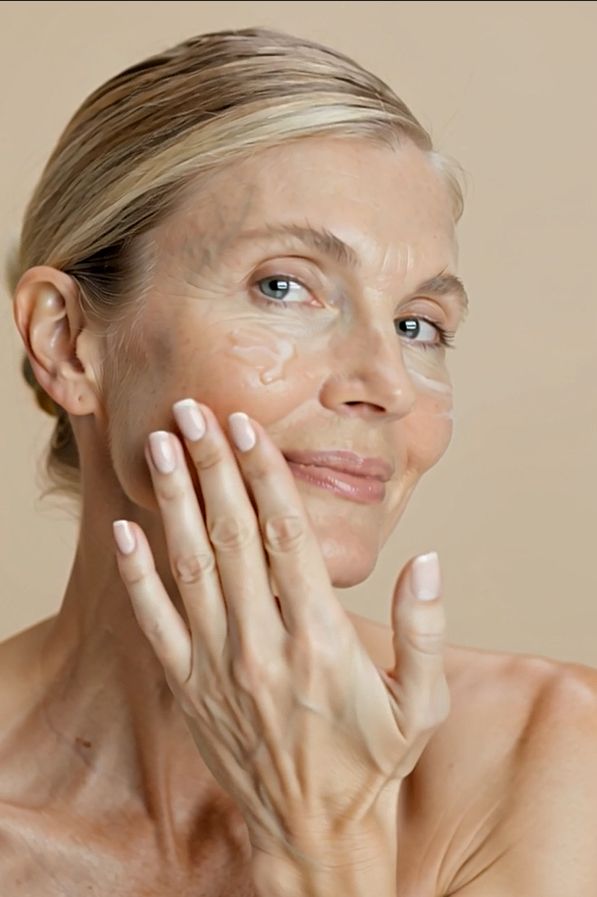 Vrouw brengt crème aan op haar gezicht. Ze glimlacht. Crème zichtbaar op de huid.