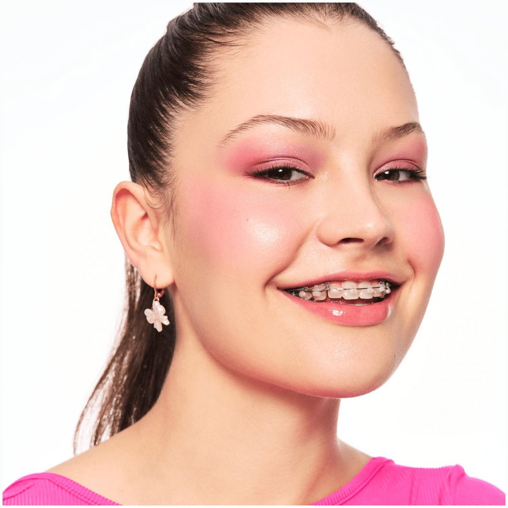 Portrait d'une jeune femme avec fard à paupières rose et appareil dentaire. Elle sourit.