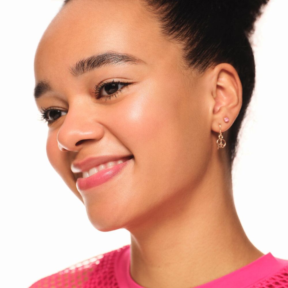 Portrait d'une femme souriante. Effet d'highlighter ciblé sur la peau. Boucles d'oreilles peace.