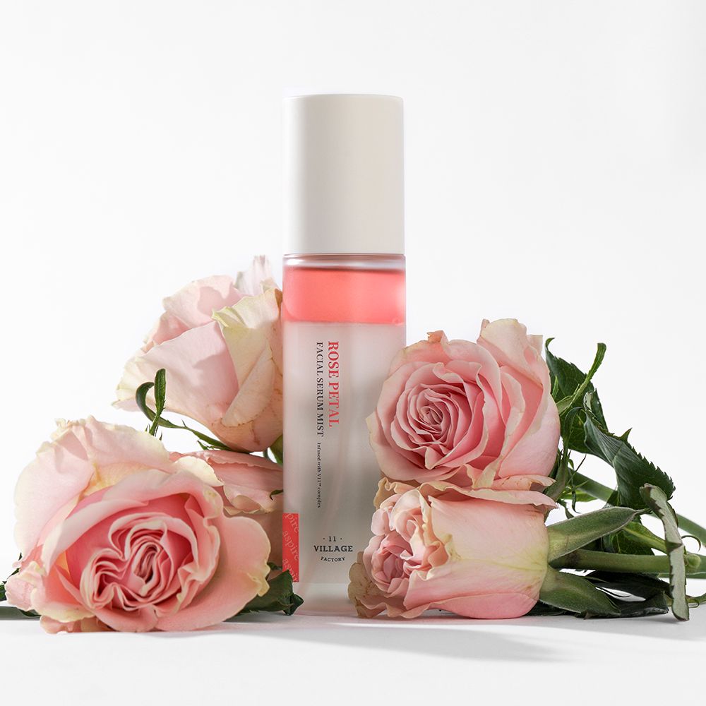 Gezichtsserumspray met rozen. Opschrift: ROSE PETAL FACIAL SERUM MIST. Omringd door rozen.
