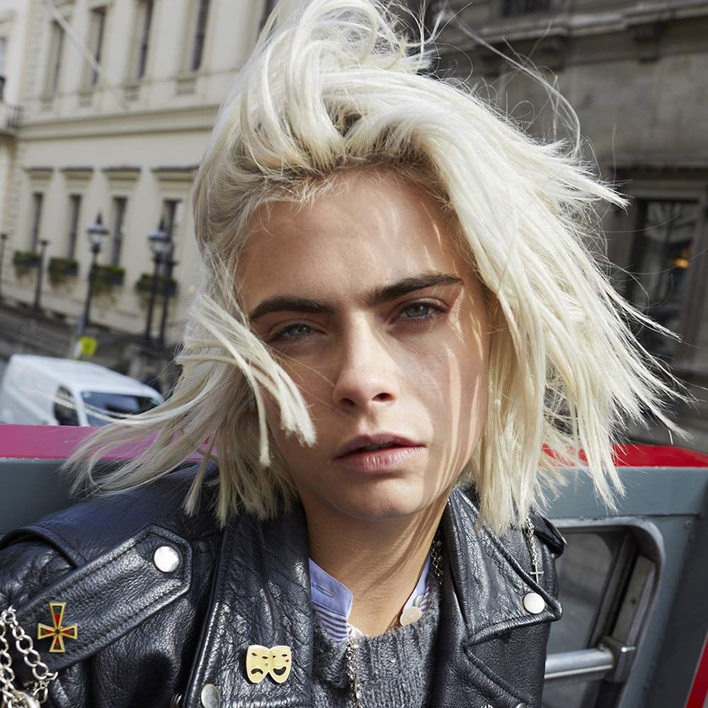 Portrait d'une femme aux cheveux blonds. Elle porte une veste en cuir noire avec des épingles.