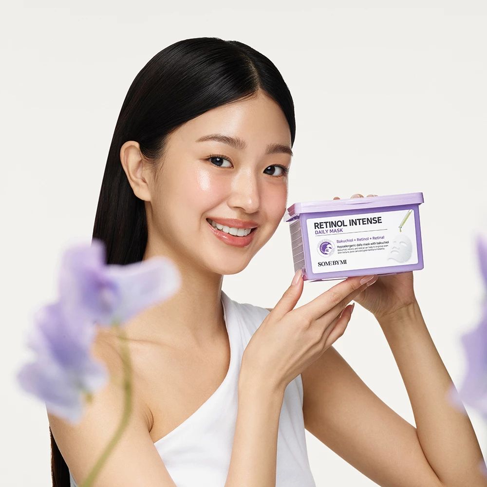 Een vrouw houdt een paars bakje vast met de tekst Retinol Intense Daily Mask. Merk: SOMEBYMI. Ze lacht.