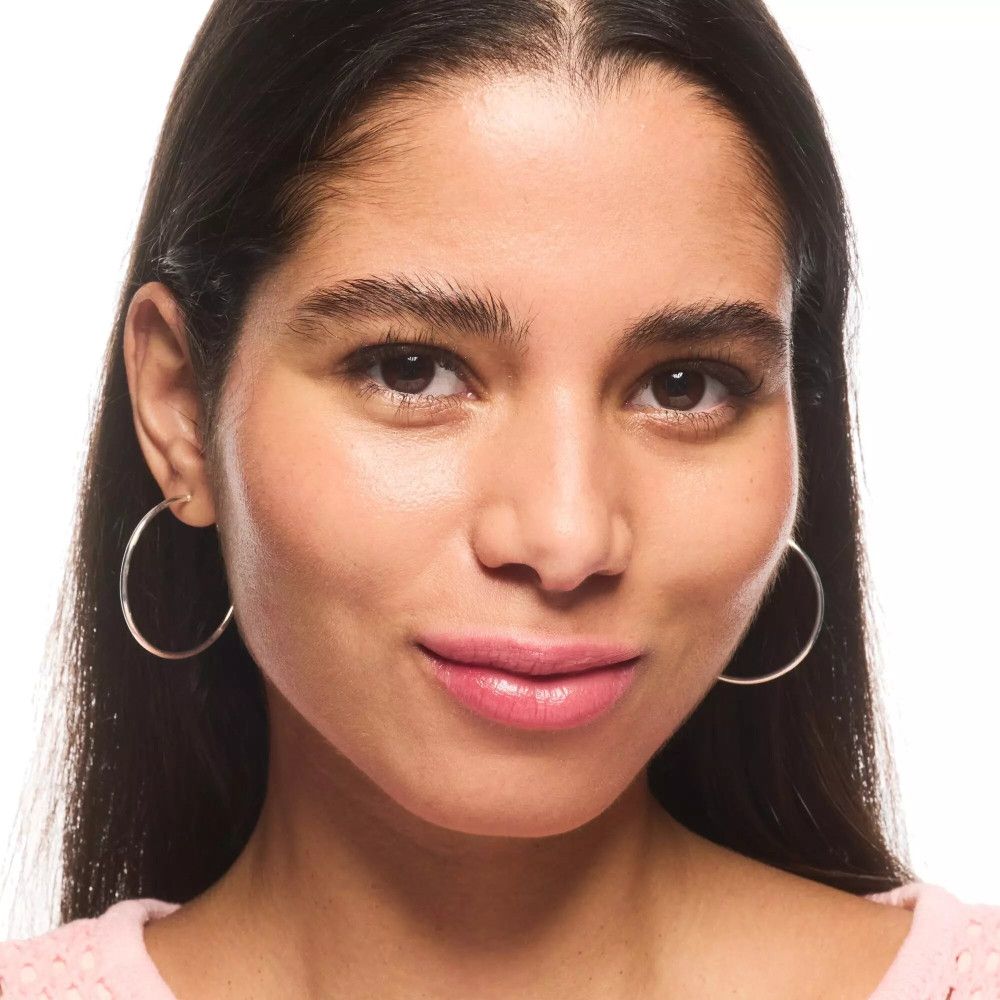 Portrait d'une femme aux cheveux foncés et créoles argentées. Elle porte du rouge à lèvres rose.