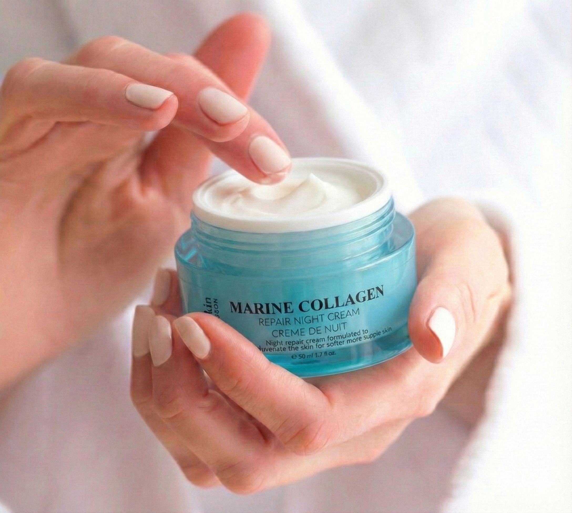Handen houden een pot Marine Collagen nachtcrème vast. Crème wordt met vinger genomen. Blauw glas, zilveren deksel. Tekst: Marine Collagen.