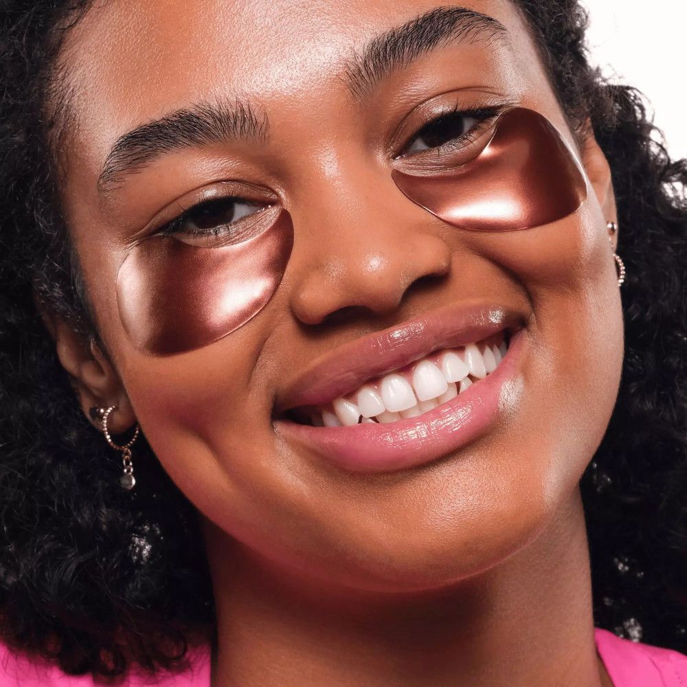 Gros plan d'une femme avec des patchs pour les yeux. Patchs en forme d'yeux, brillants, bruns. La femme sourit.