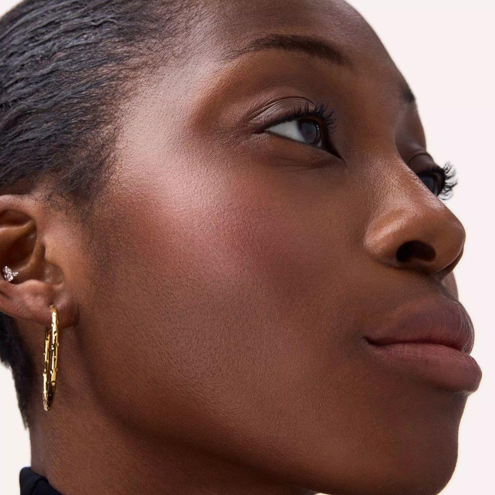 Gros plan d'un visage avec du fard à joues sur les joues. La personne porte des boucles d'oreilles.