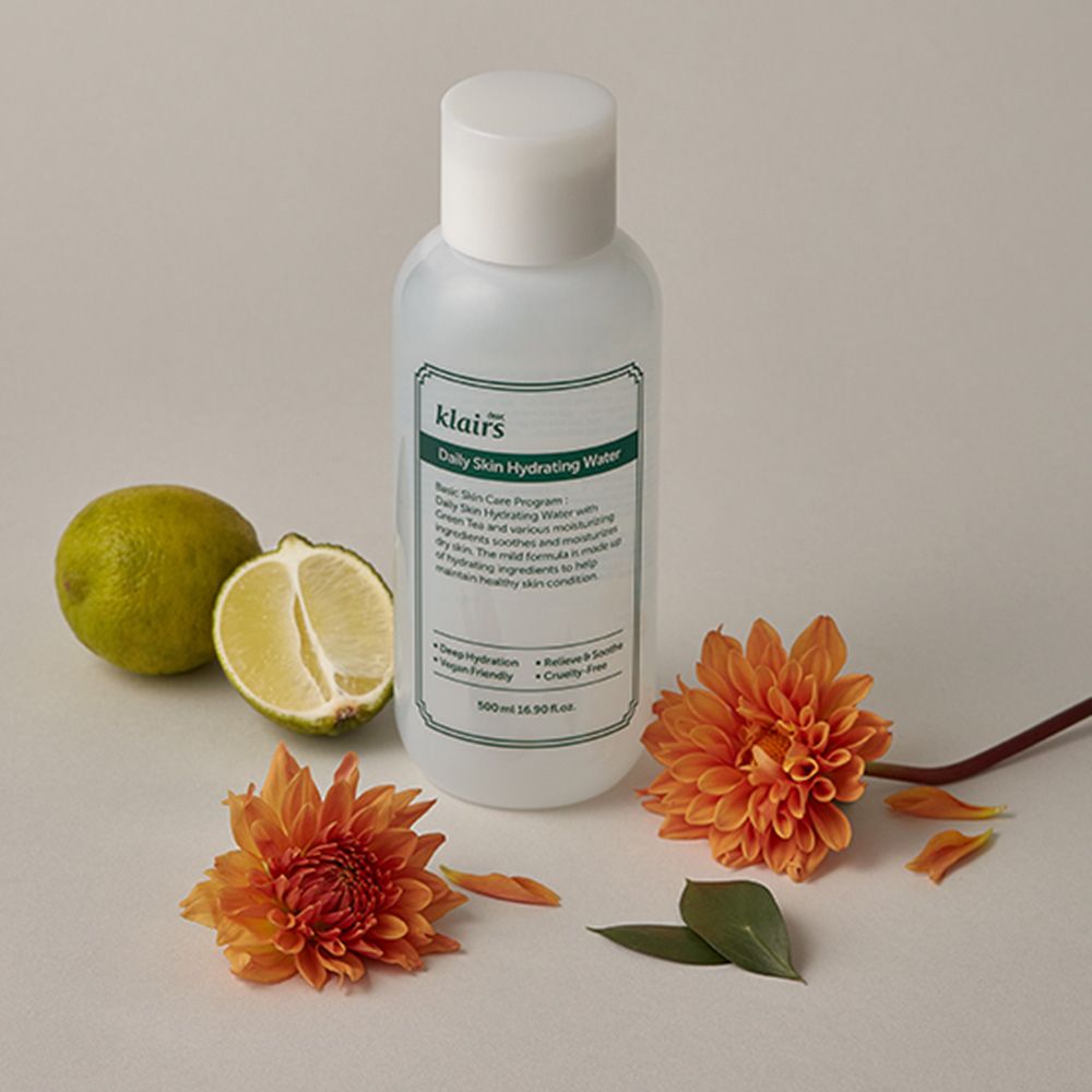 Witte fles met groen etiket, naast limoen en oranje bloemen. Tekst: klairs, Daily Skin Hydrating Water.