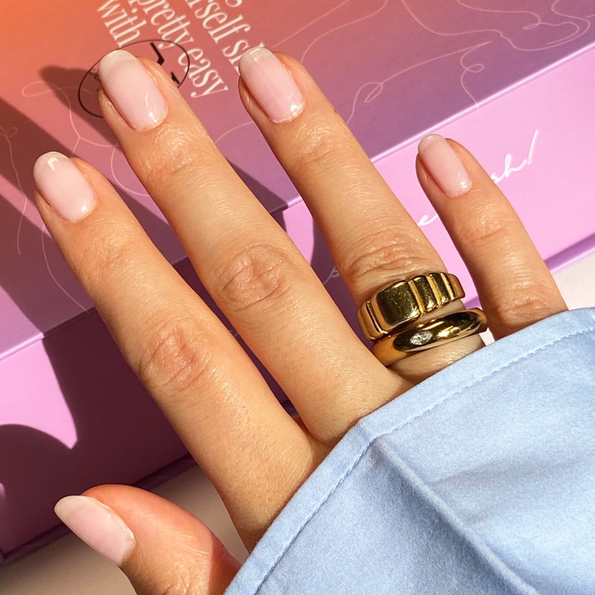 Hand met gelakte nagels. Gouden ringen. Lichte nagellakkleur. Blauwe mouw.