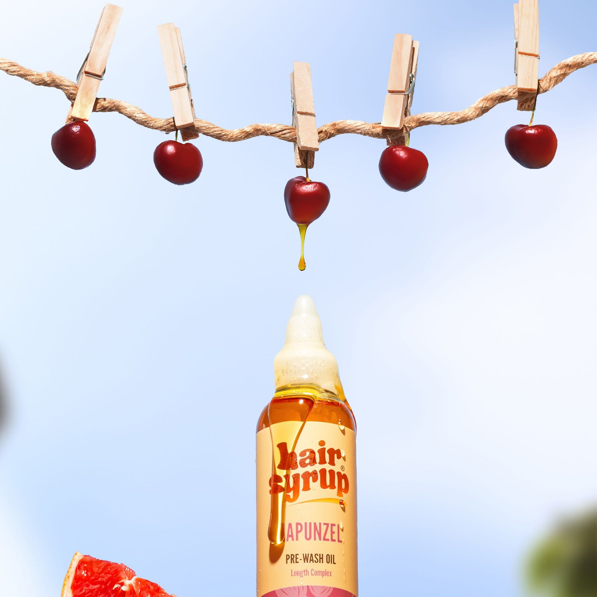 Hair Syrup Rapunzel Pre-Wash Oil fles met kersen aan wasknijpers. Gele vloeistof druppelt.