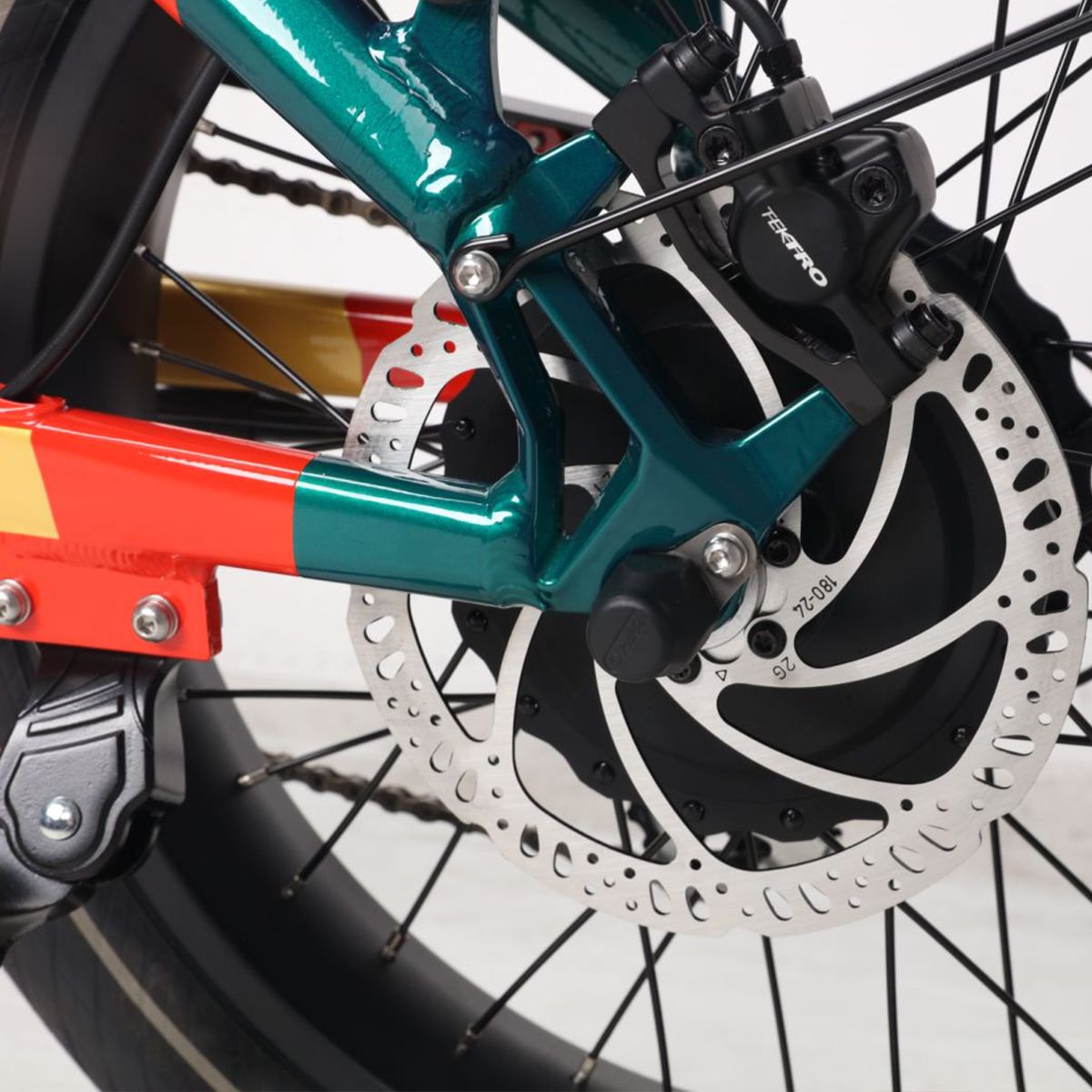 Frein arrière d'un vélo électrique. Frein à disque, détails noirs. Design vert-rouge. Logo TEKTRO visible.