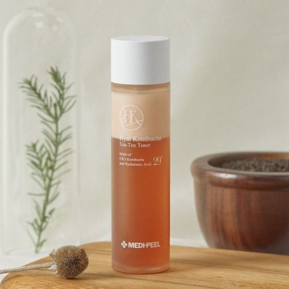 Hyal Kombucha Tea-Tox Toner fles op houten plank, naast planten en kom.