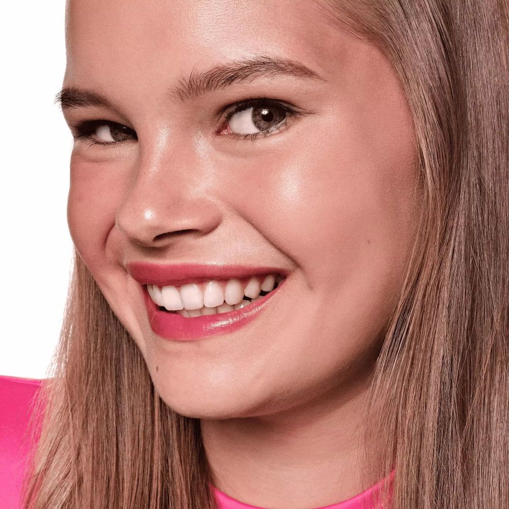 Portrait d'une femme souriante. Lèvres avec rouge à lèvres rouge. Haut rose. Peau claire, cheveux blonds.