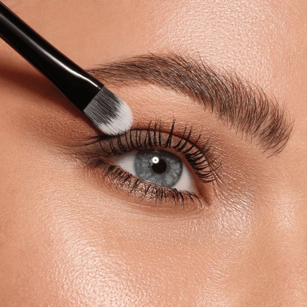 Close-up van een oog met oogschaduwkwast. Kwast met witte borstel.