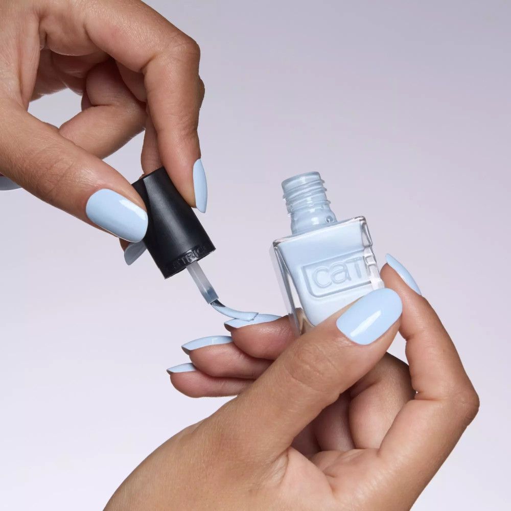 Mains tenant un flacon de vernis à ongles et un pinceau. Vernis à ongles bleu clair. Marque Catrice.
