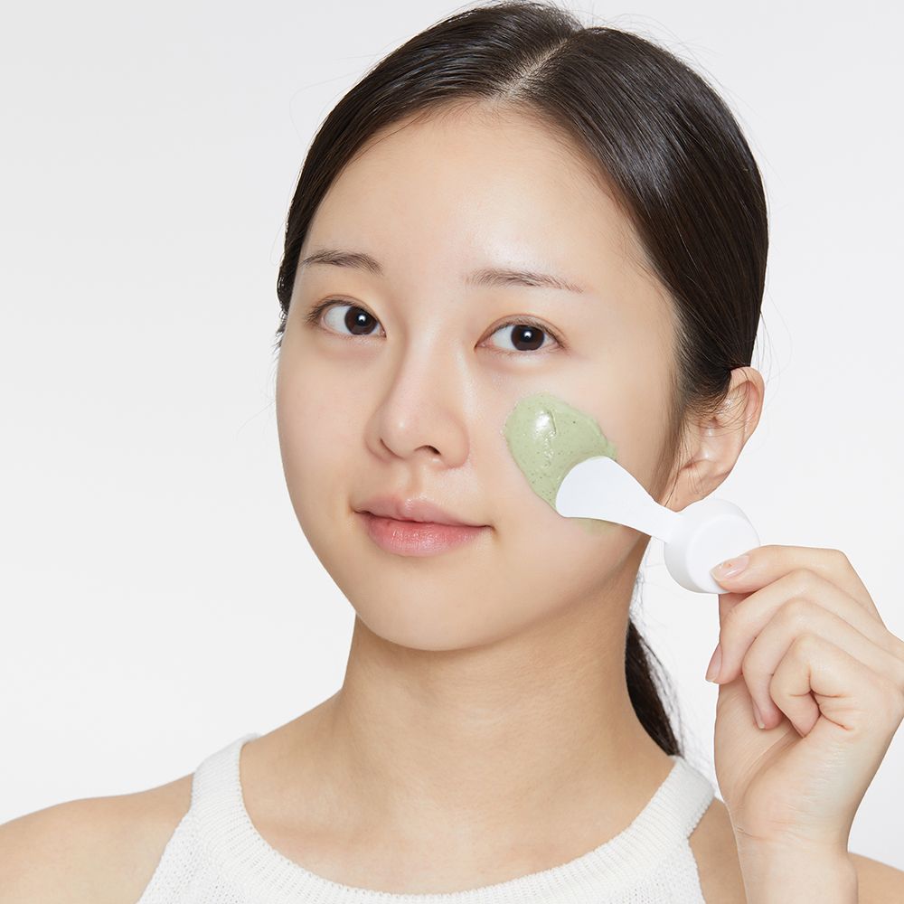Femme avec masque sur le visage. Une spatule applique le masque vert.