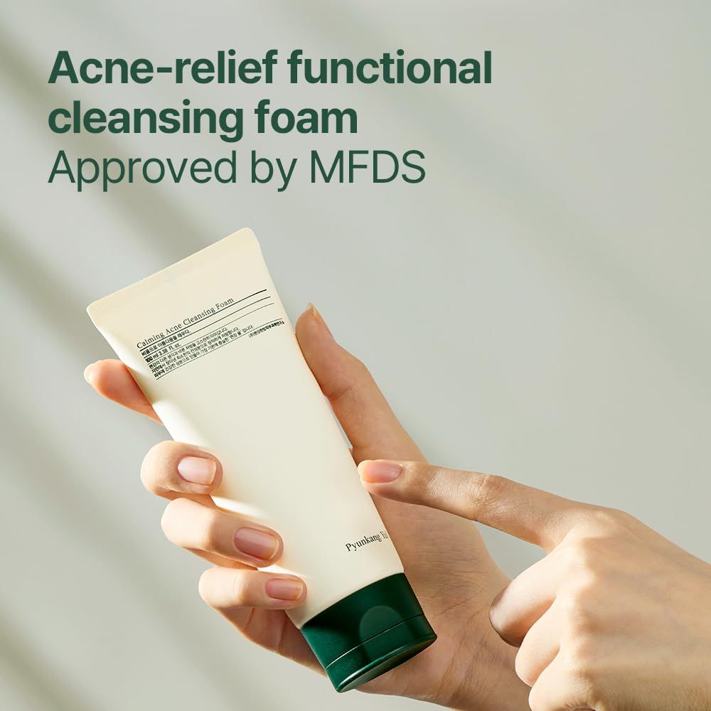 Main tenant un tube de mousse nettoyante. Boîtier blanc, bouchon vert. Texte: Acne-relief functional cleansing foam, MFDS.
