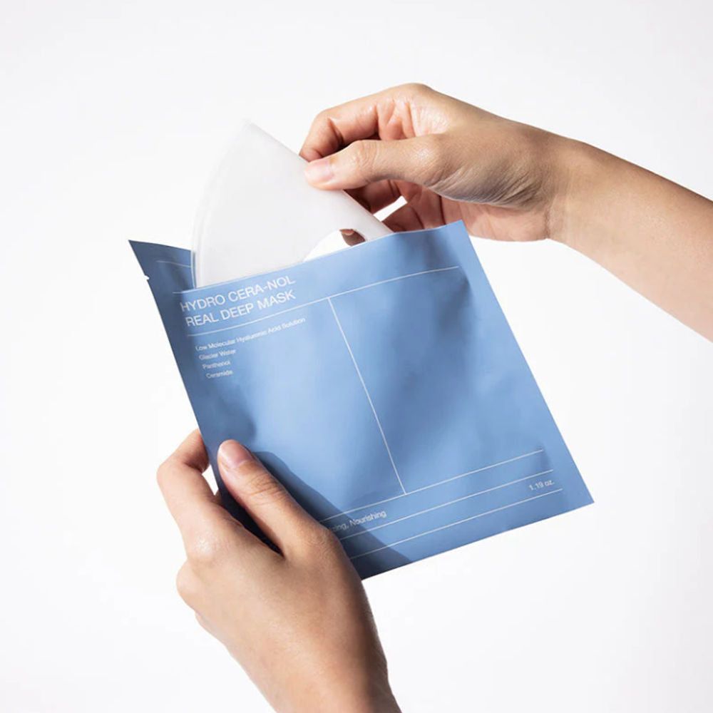 Mains ouvrant un sachet bleu. Un masque blanc est retiré. Sur l'emballage, "Biodance Hydro Cera Nol Real Deep Mask".
