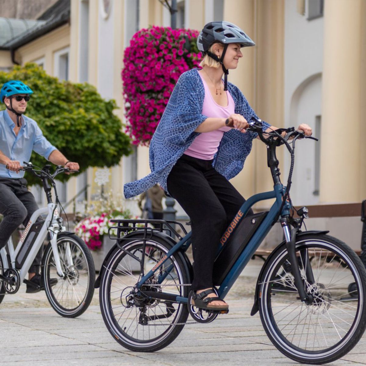 Deux personnes font du vélo électrique bleu et blanc. Casques, environnement urbain.