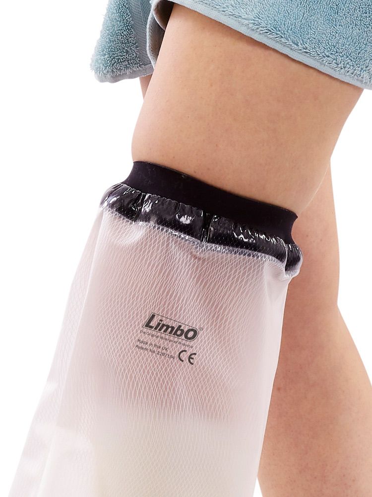 Gros plan sur la protection de douche sur la jambe. Bordure noire, matériau blanc. Nom du produit et marquage CE visibles.
