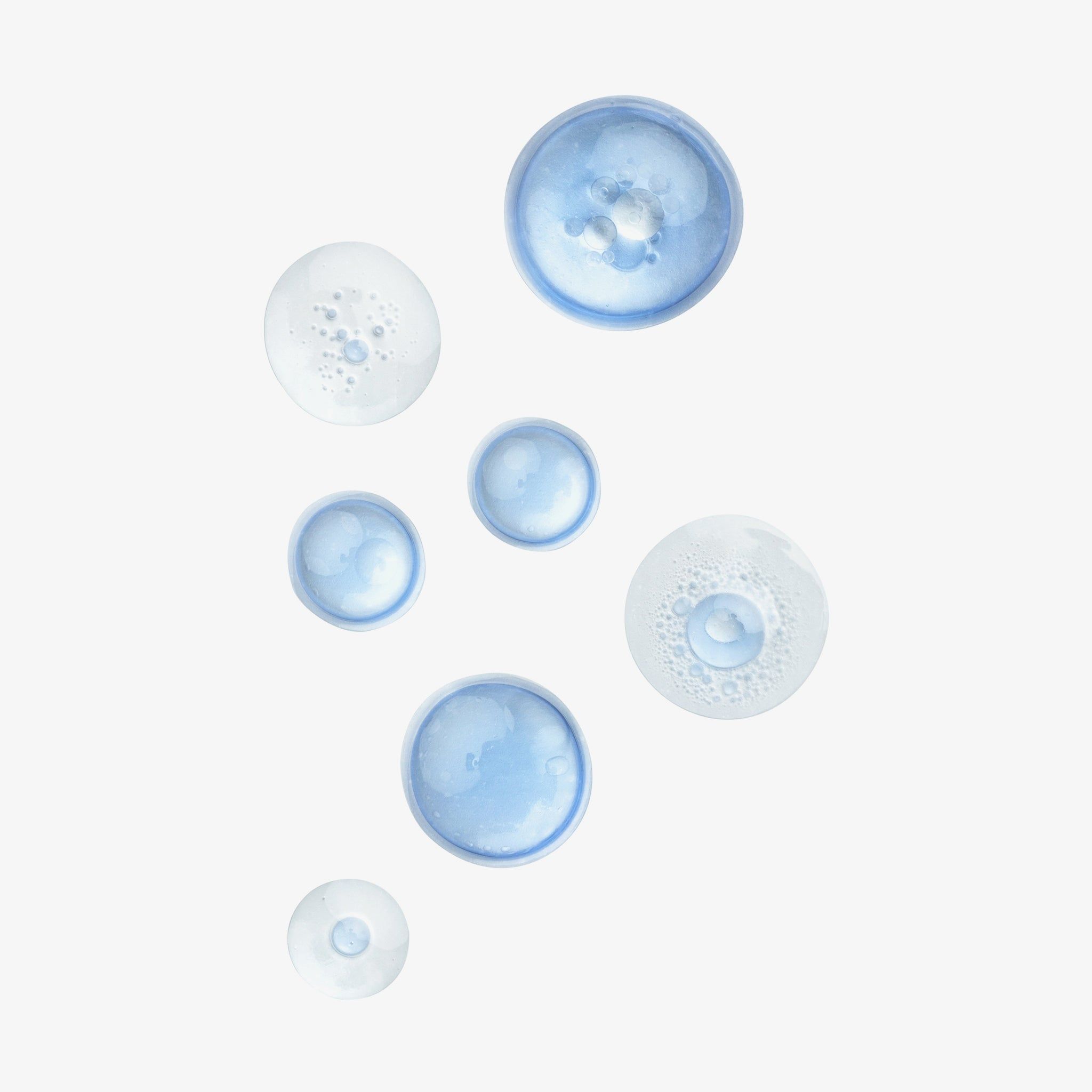 Plusieurs gouttes bleues et transparentes sur fond blanc. Différentes tailles et formes. Certaines gouttes sont mousseuses.