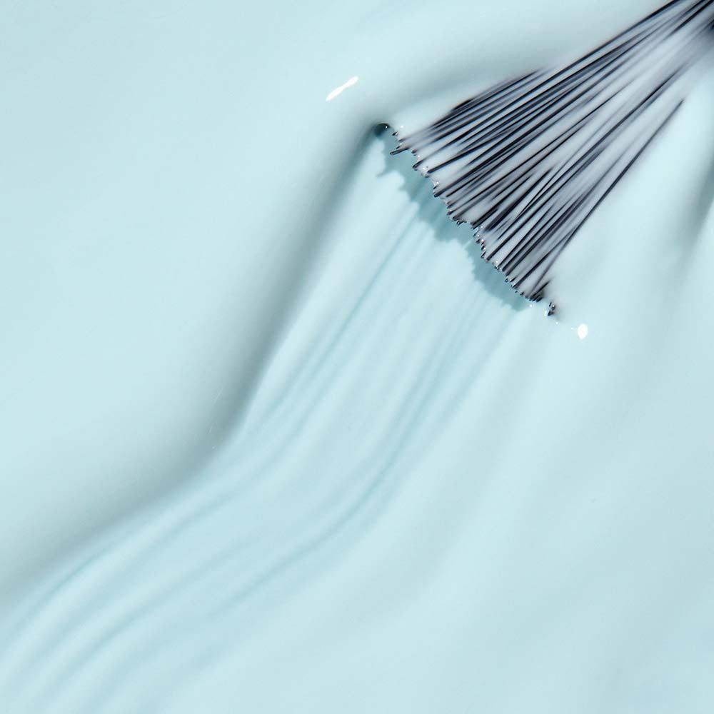 Vernis à ongles bleu clair avec pinceau. Le pinceau est plongé dans le vernis, créant une texture ondulée. Vue rapprochée.