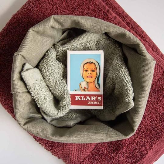 Verpakking in handdoek. Rechthoekige doos met vrouw, in handdoek gelegd. Rode tekst: KLAR'S DAMENSEIFE.