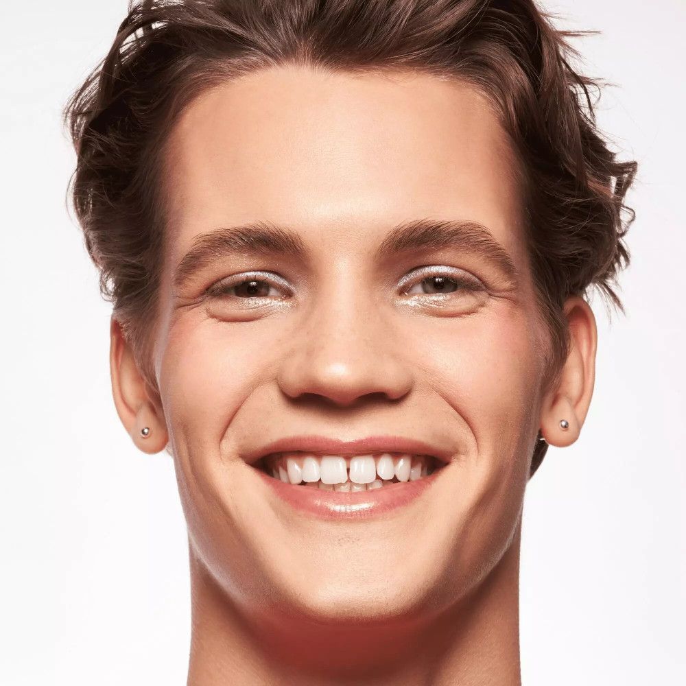 Portrait d'un homme à la peau claire. Il sourit. Il porte des boucles d'oreilles.