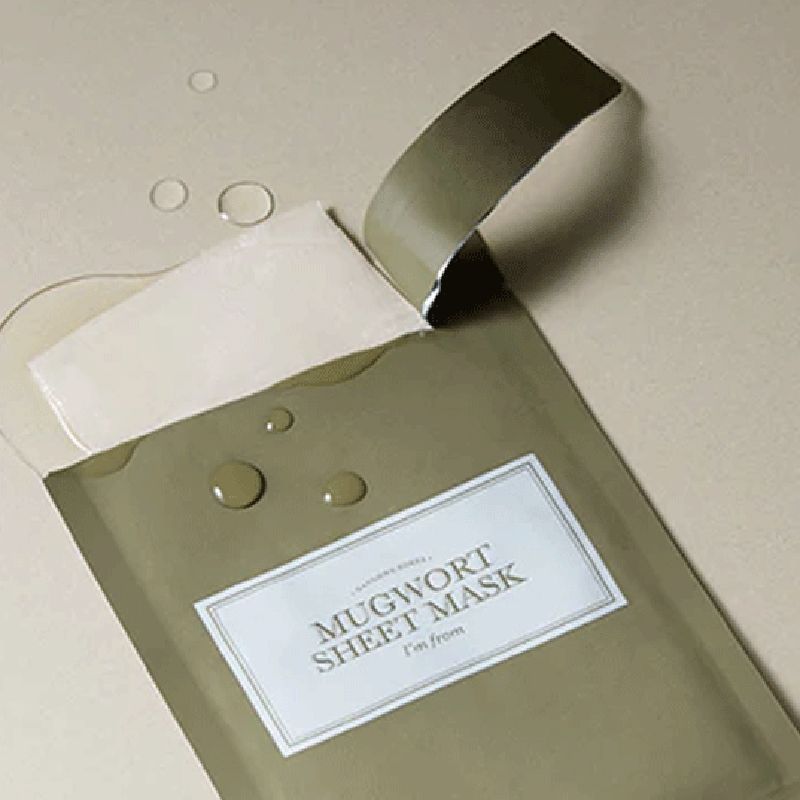Emballage vert avec étiquette blanche. Inscription : MUGWORT SHEET MASK, i'm from. Une feuille est retirée, gouttes d'eau.