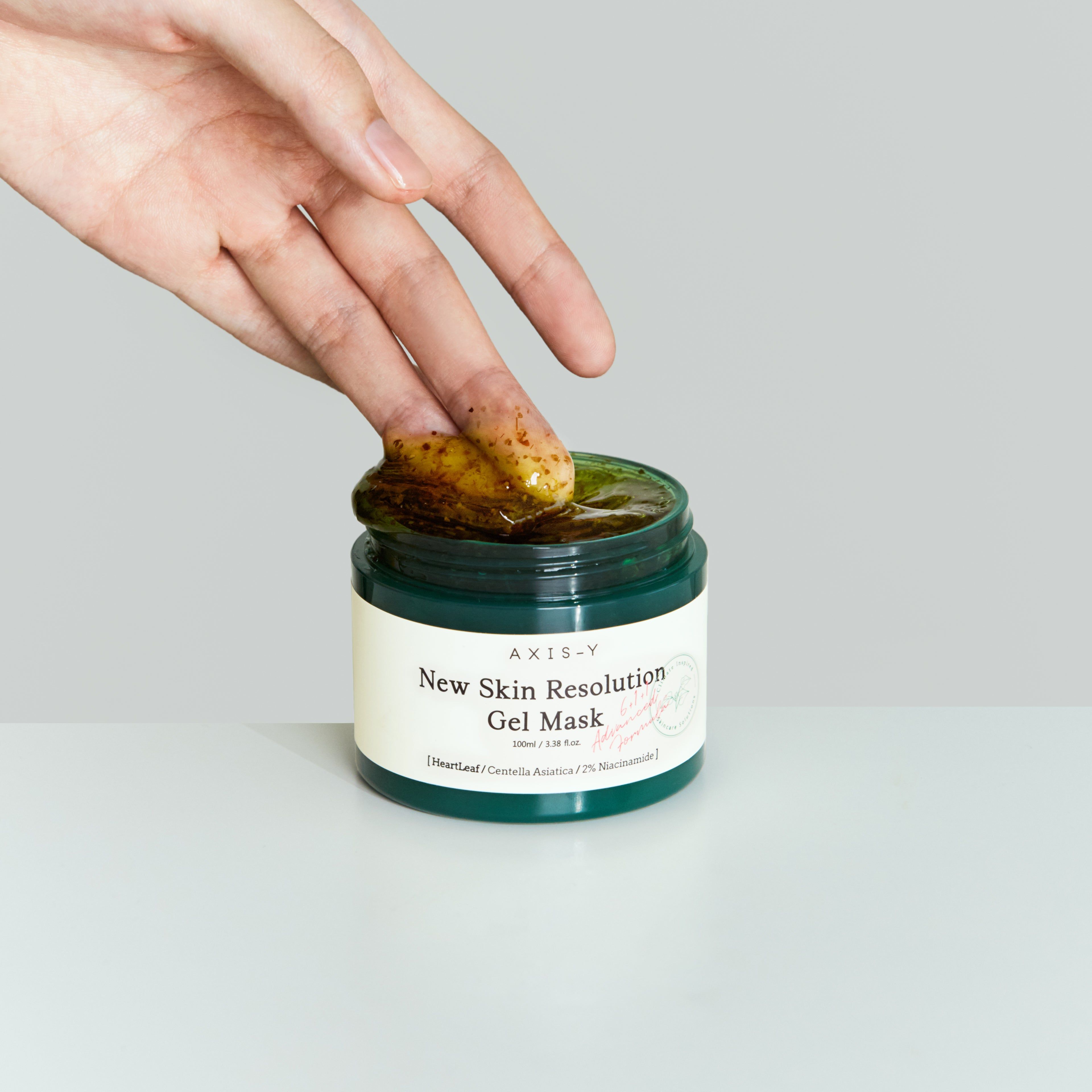 Hand doopt vinger in groen gelmasker. Opschrift: New Skin Resolution Gel Mask.