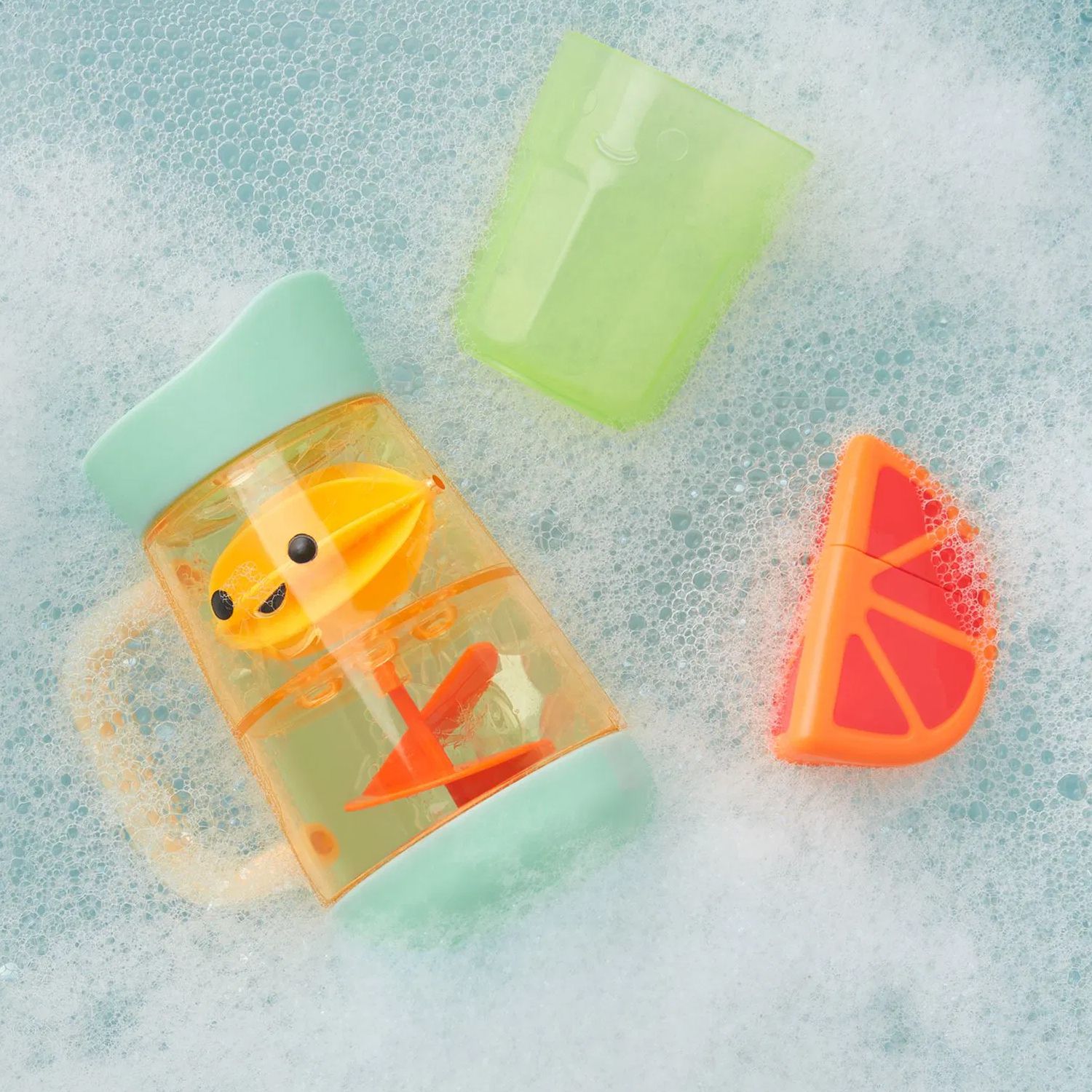 Badspeelgoedset in het water. Kan, beker en oranje speelgoed. Kan met handvat en draaiend deel. Groene beker. Sinaasappel in twee helften.