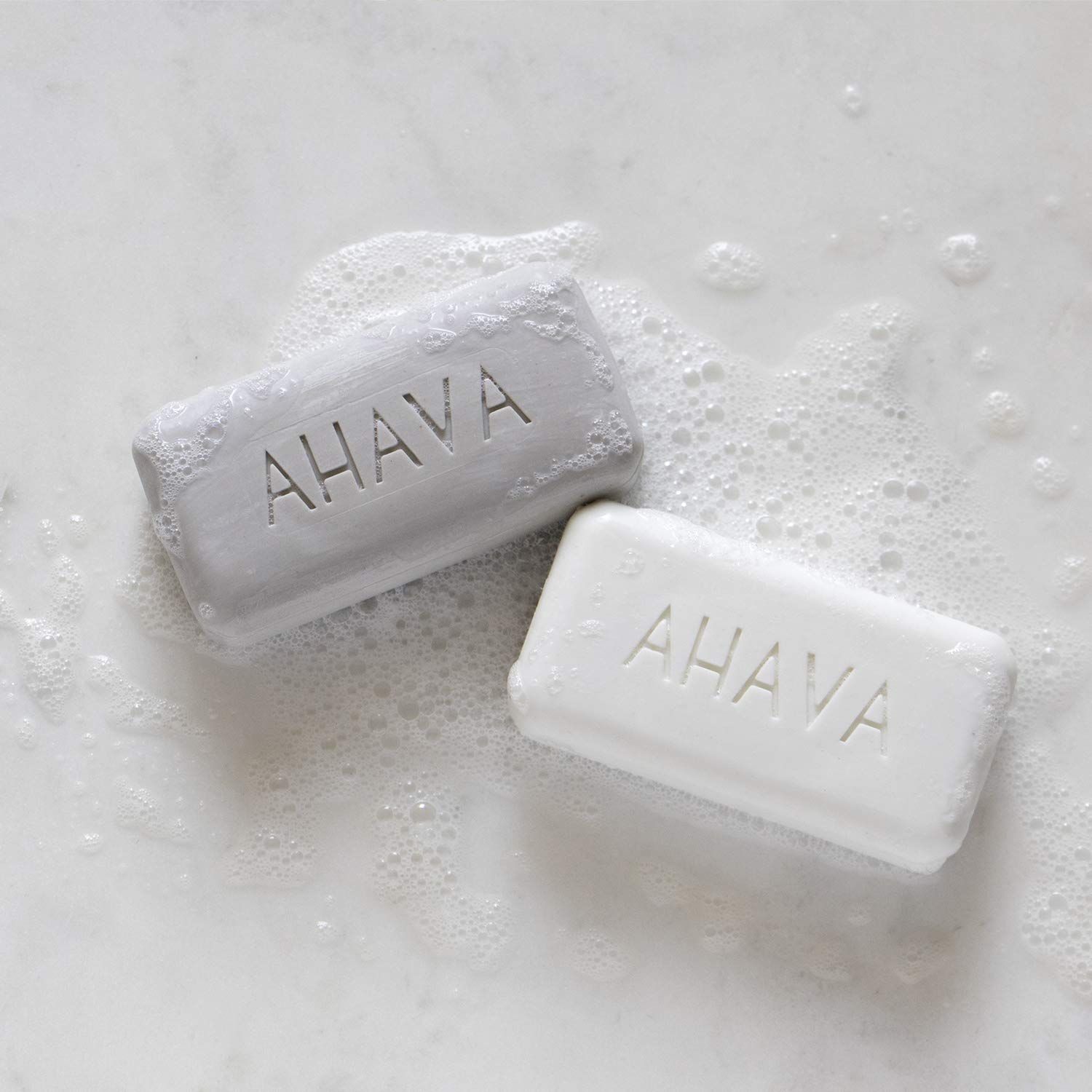 Twee AHAVA-zeepjes, één grijs, één wit, in schuim.